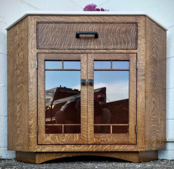Woodworkers crafted a rustic wooden cabinet with glass-paneled doors showcasing intricate woodworking skills.