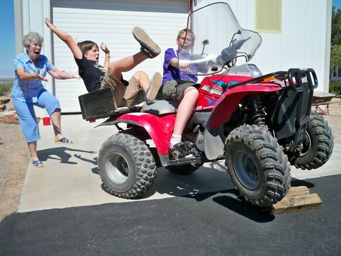 Two kids on a red ATV with front wheels off the ground, while a woman behind reacts, a funny and interesting perfect timing pic.