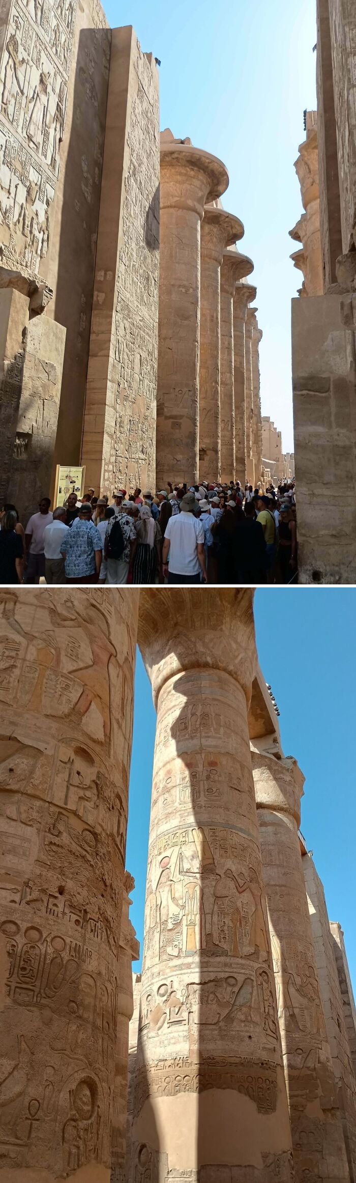 Crowd exploring ancient Egypt ruins with towering stone columns covered in detailed hieroglyphics and carvings under clear sky.