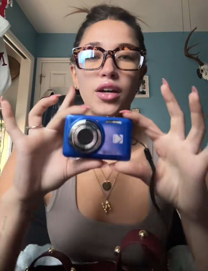 Young woman wearing glasses holding a compact digital camera, sharing Christmas gifts people highly recommend.