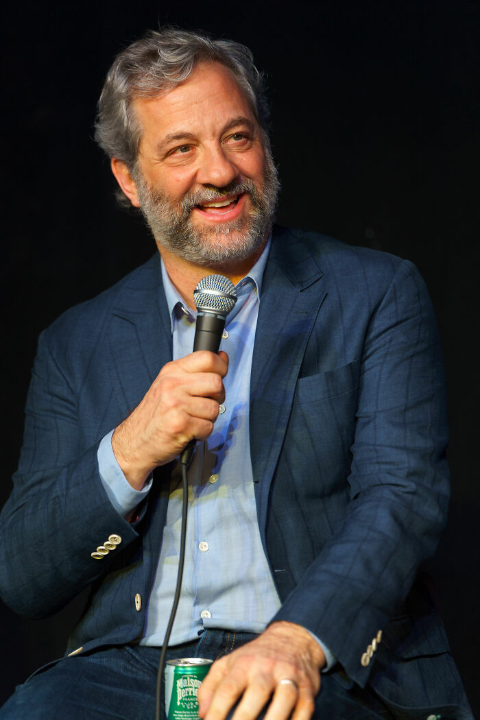 Judd Apatow holding a microphone, smiling and speaking during an event, wearing a blue suit jacket.