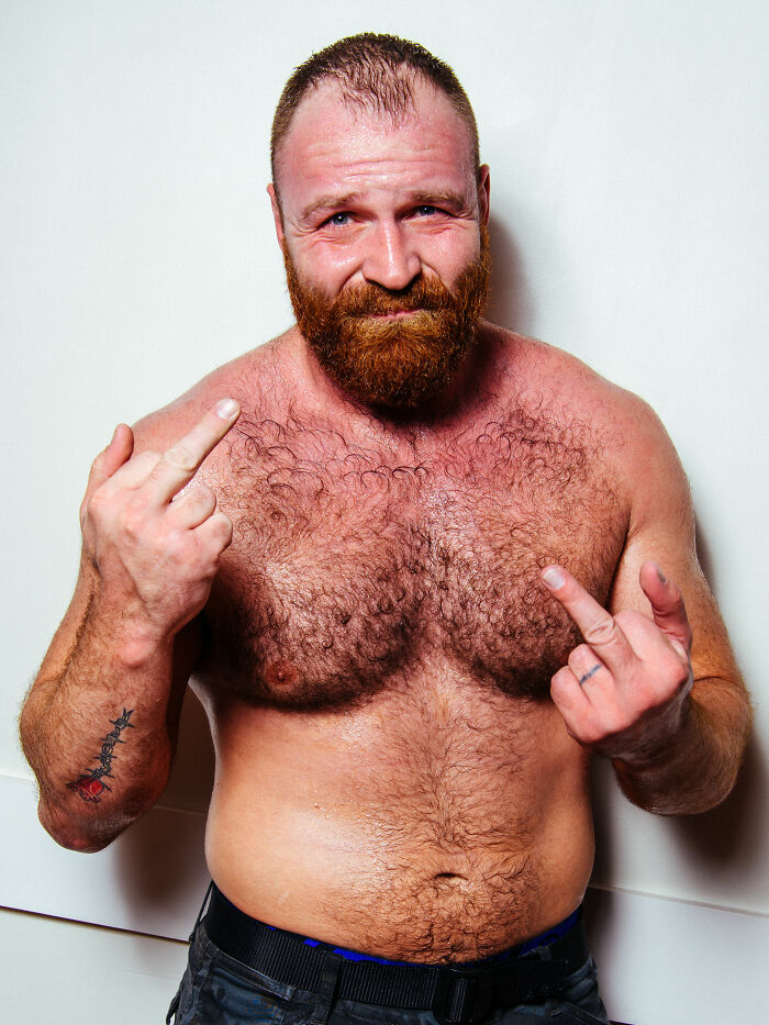 Jon Moxley shirtless with a beard showing middle fingers and a confident expression against a plain white background.