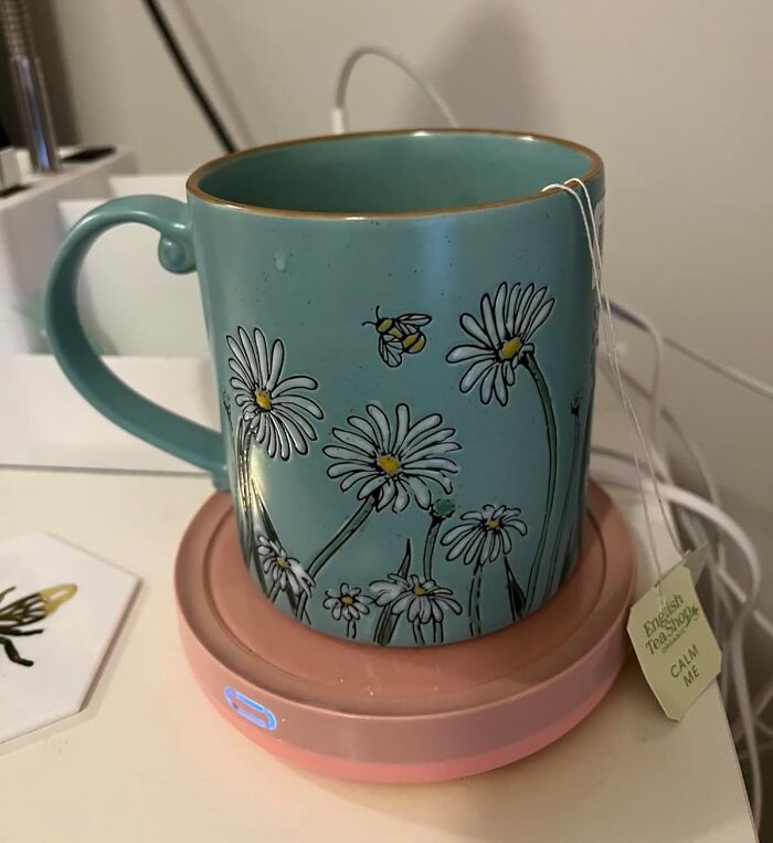 Blue ceramic mug with daisies and bee design on a pink warmer, ideal gift for teacher with caffeine a*******n and patience.