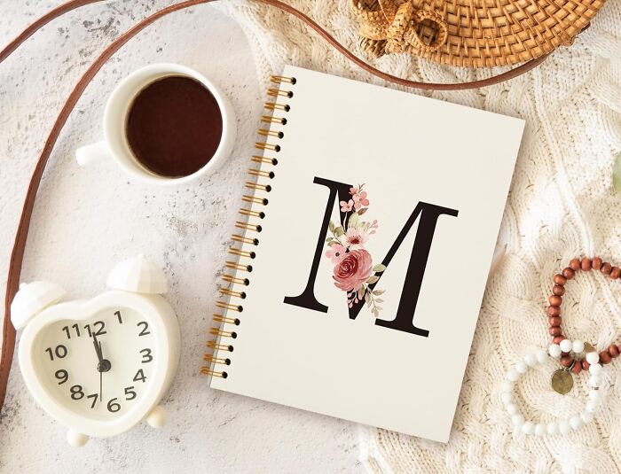 Flat lay of caffeine and gifts including a coffee cup, floral monogram notebook, and cozy accessories for patient teacher gifts.