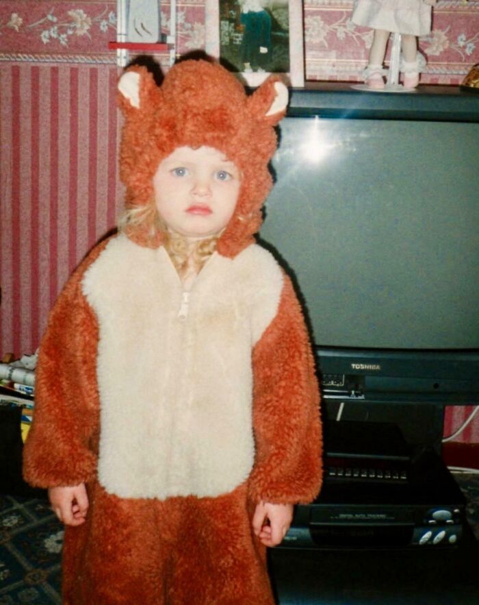 Child in a fuzzy animal costume standing in a living room, part of hilariously awkward childhood photos collection.