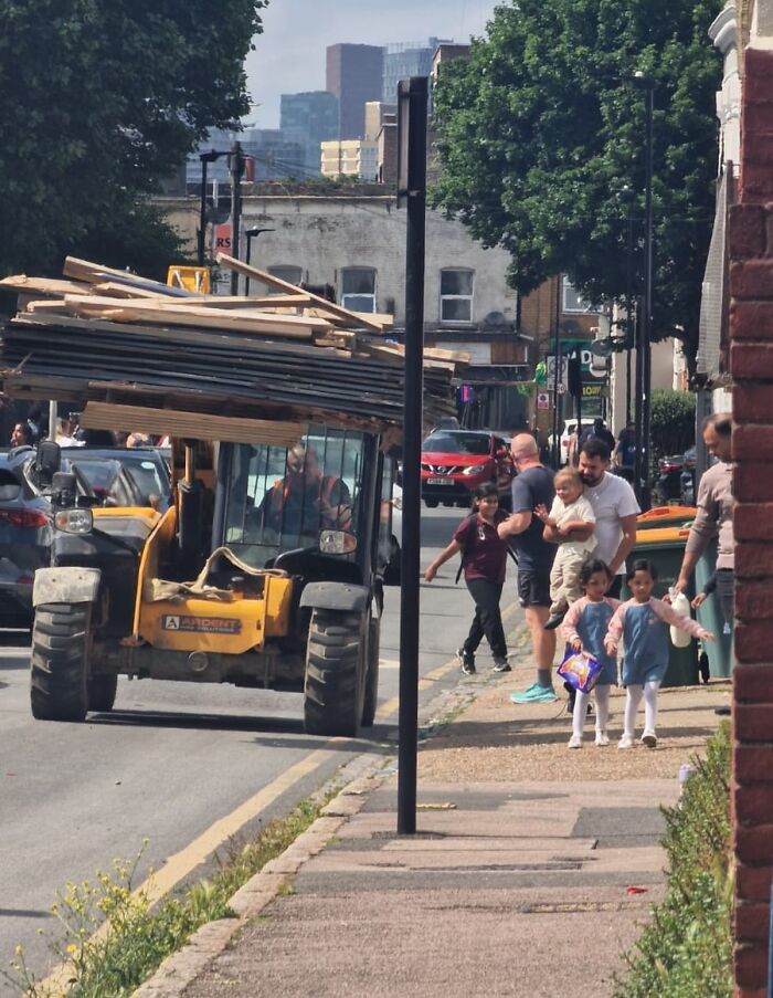 Construction vehicle carrying an unstable load of wood dangerously close to pedestrians on a busy urban street.