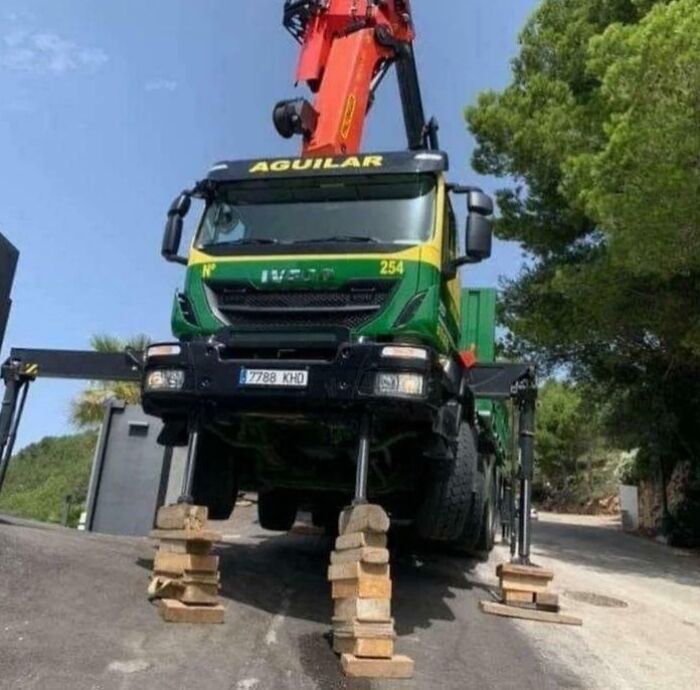 Construction truck dangerously elevated on unstable wooden blocks, showcasing employees blatantly ignoring safety protocol on a slope.