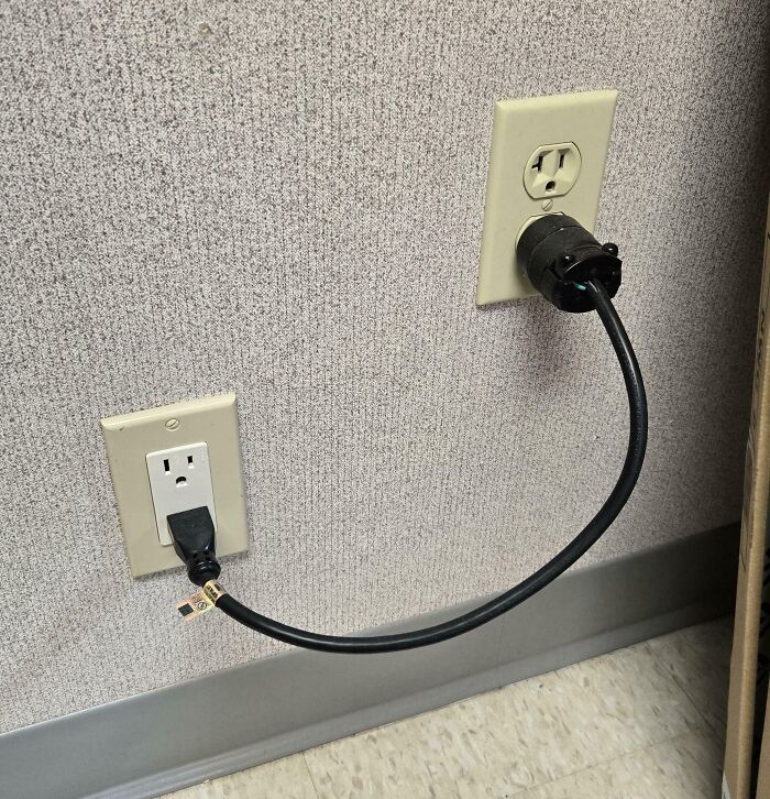 Extension cord dangerously connected between two wall outlets ignoring safety protocol in a workplace setting.
