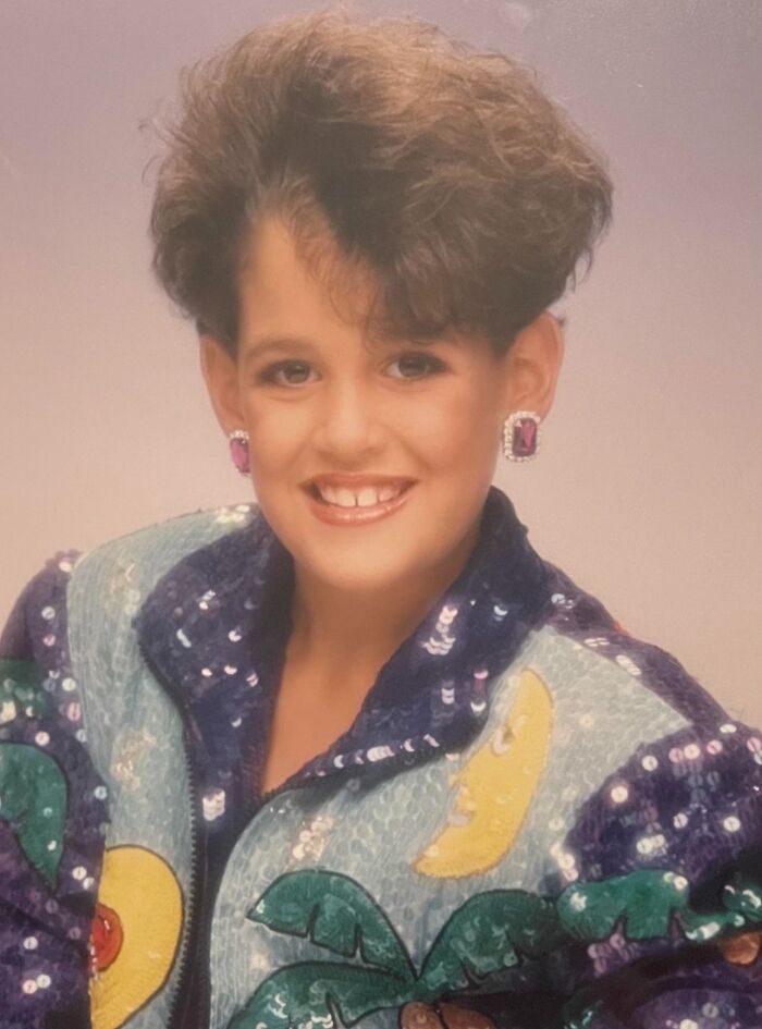 Child smiling in a sequined jacket with exaggerated 80s hairstyle and large earrings in a hilariously awkward childhood photo.