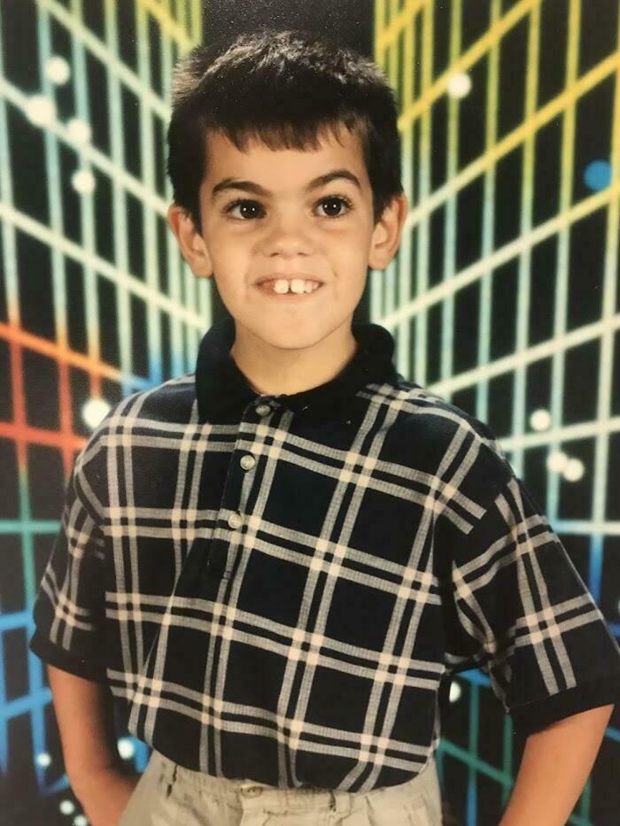 Young boy in a plaid shirt posing awkwardly against a colorful geometric background in a hilarious childhood photo.