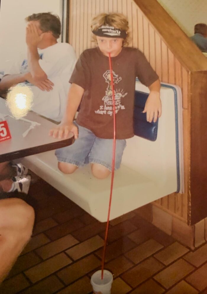 Child using an extremely long straw to drink from a cup, capturing a hilariously awkward childhood photo moment.