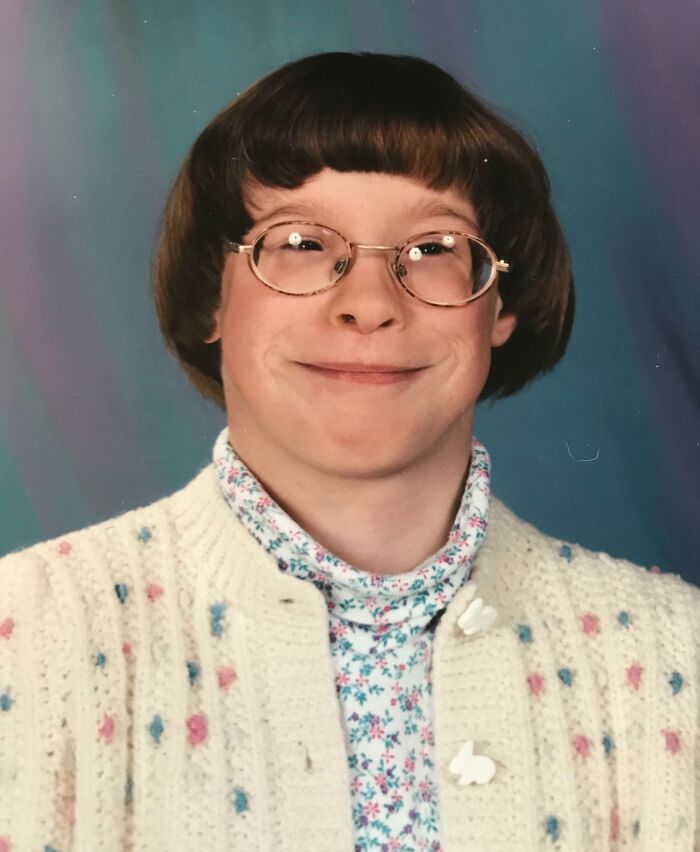 Awkward childhood photo of a smiling child wearing glasses, a floral shirt, and a cream knitted sweater.