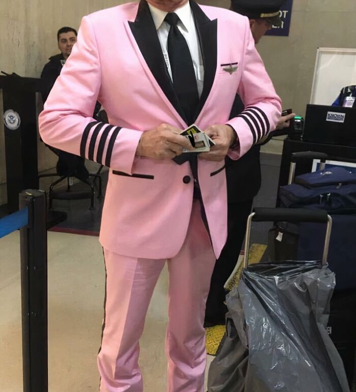 Employee wearing a pink suit with black stripes at an airport, part of a collection of employees with jokes and pranks.
