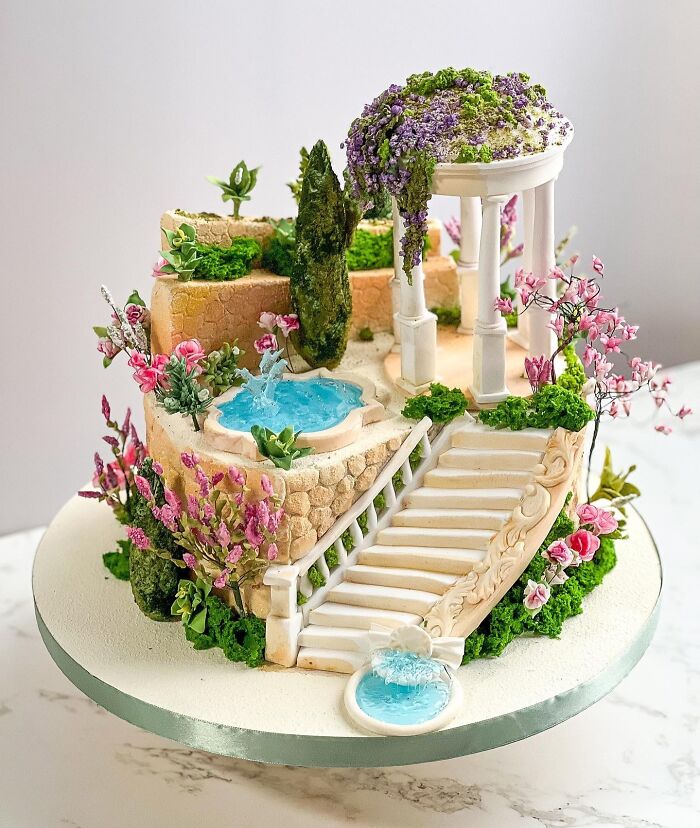 Intricately designed cake featuring a garden scene with stairs, water fountains, and vibrant flowers showcasing masterful cake creativity.