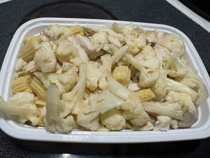Meal with cauliflower, baby corn, and chicken pieces in a white container, showcasing an outrageous meal that looks nothing like menu photos.