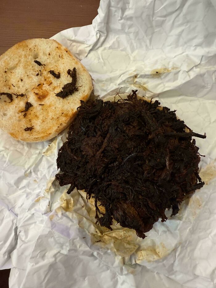 Burnt and unappetizing burger patty with a plain bun on crumpled white paper showing outrageous meal fail.