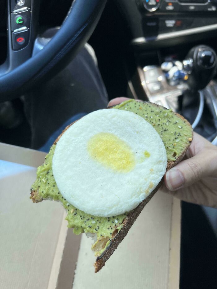 Half-eaten meal in a car showing an avocado toast with a poorly made egg resembling a white disc, meal looks nothing like menu photos.