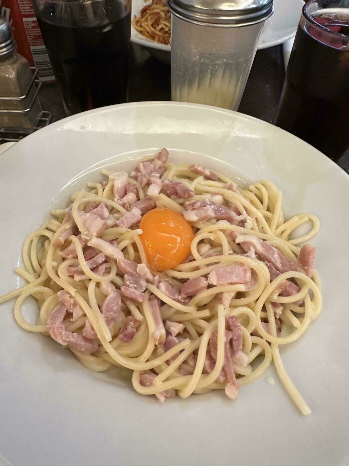 Plate of pasta with scattered ham and a raw egg yolk, an example of outrageous meals that look nothing like menu photos.
