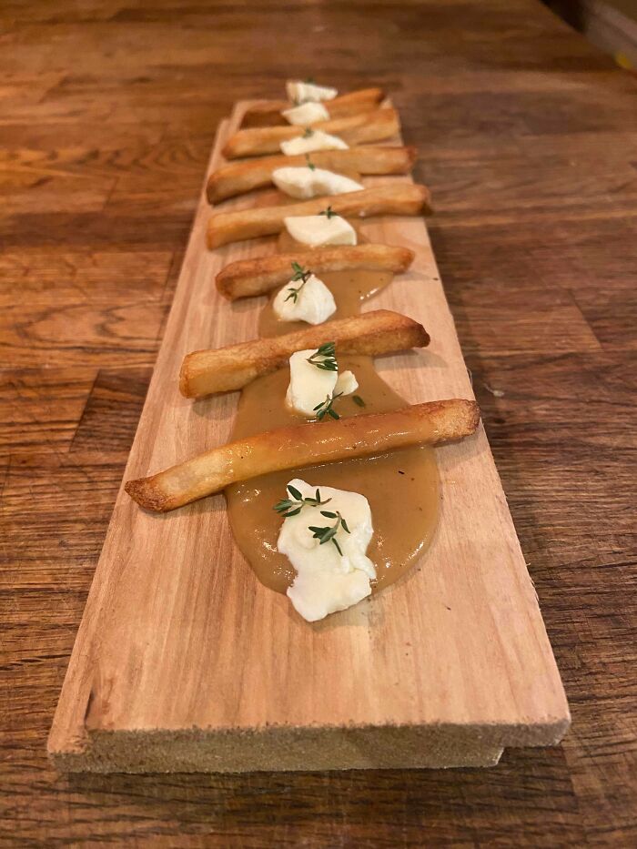 French fries arranged on a wooden board with dollops of sauce and herbs, an example of outrageous meals.