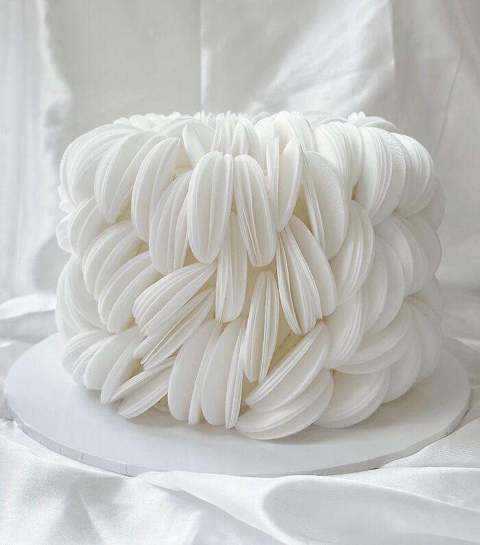 White masterfully crafted cake with intricate petal-like layers showcasing creativity in cake design on a white backdrop.