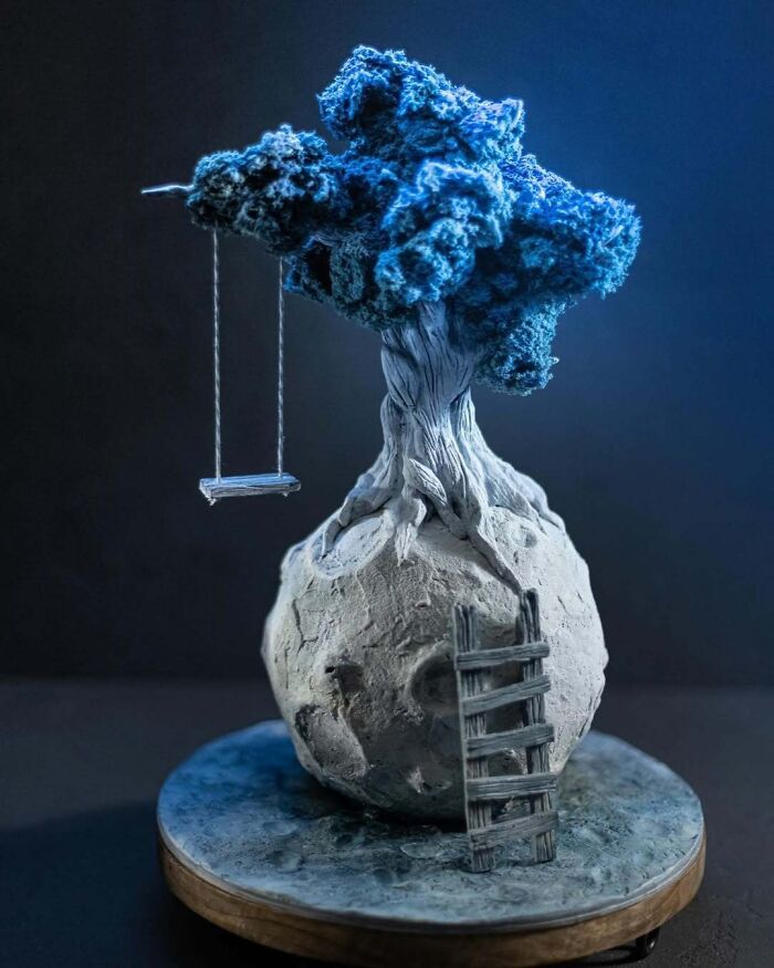 Masterfully crafted cake depicting a twisted tree with blue foliage on a textured spherical base with a ladder and swing.