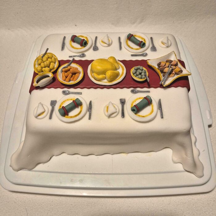 Cake designed as a detailed dinner table with plates, silverware, and food, showcasing masterfully crafted cake creativity.