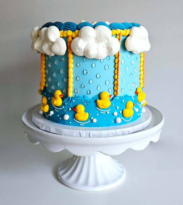 Cake decorated with clouds, raindrops, and rubber ducks on blue frosting showcasing masterfully crafted cake creativity.