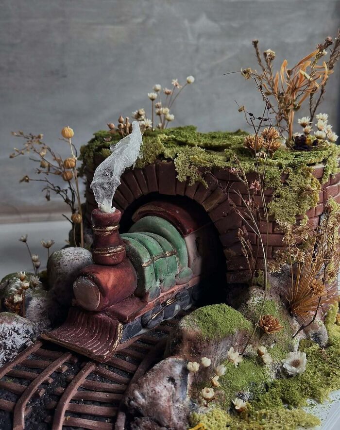 Train cake emerging from moss-covered tunnel with detailed greenery, showcasing masterfully crafted cakes and human creativity.