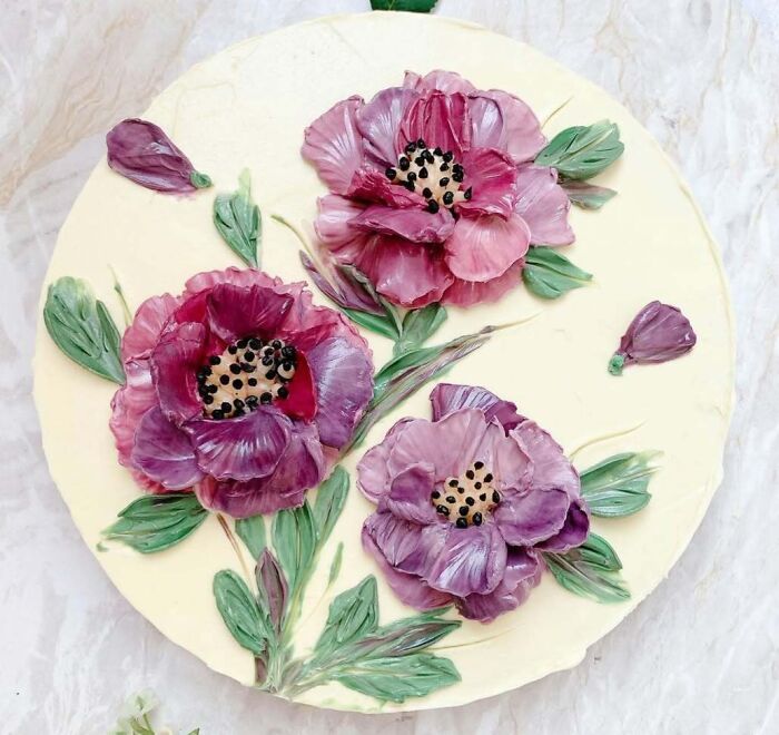 Round cake decorated with masterfully crafted purple flowers and green leaves showcasing human creativity in cake design.
