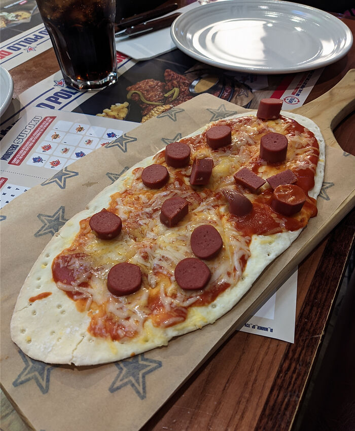 Flatbread pizza with unevenly cut hot dog pieces and cheese, illustrating outrageous meals that look nothing like menu photos.