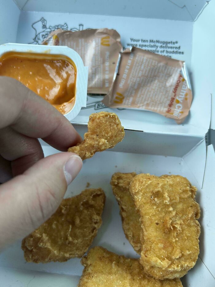 Hand holding a small chicken nugget next to larger nuggets and sauce packets, showing outrageous meals not matching menu photos.