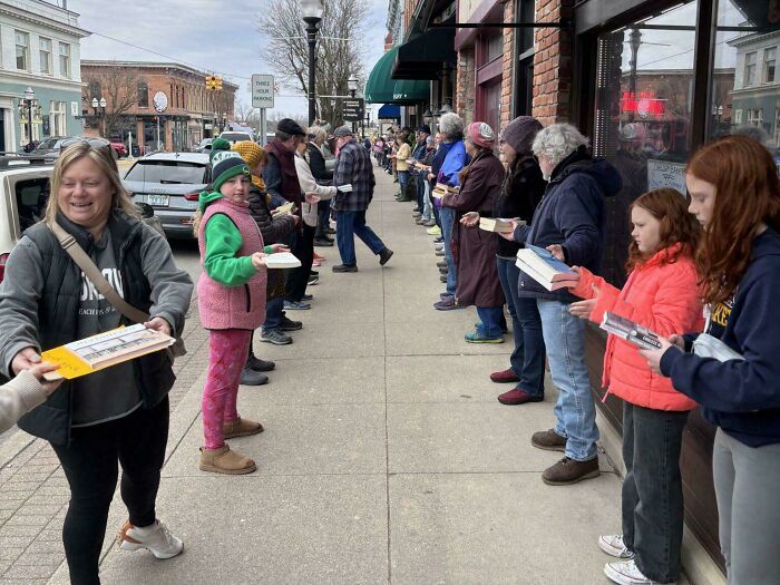 People lined up outdoors in a social setting, engaging in an activity involving books or papers in a math problem challenge.