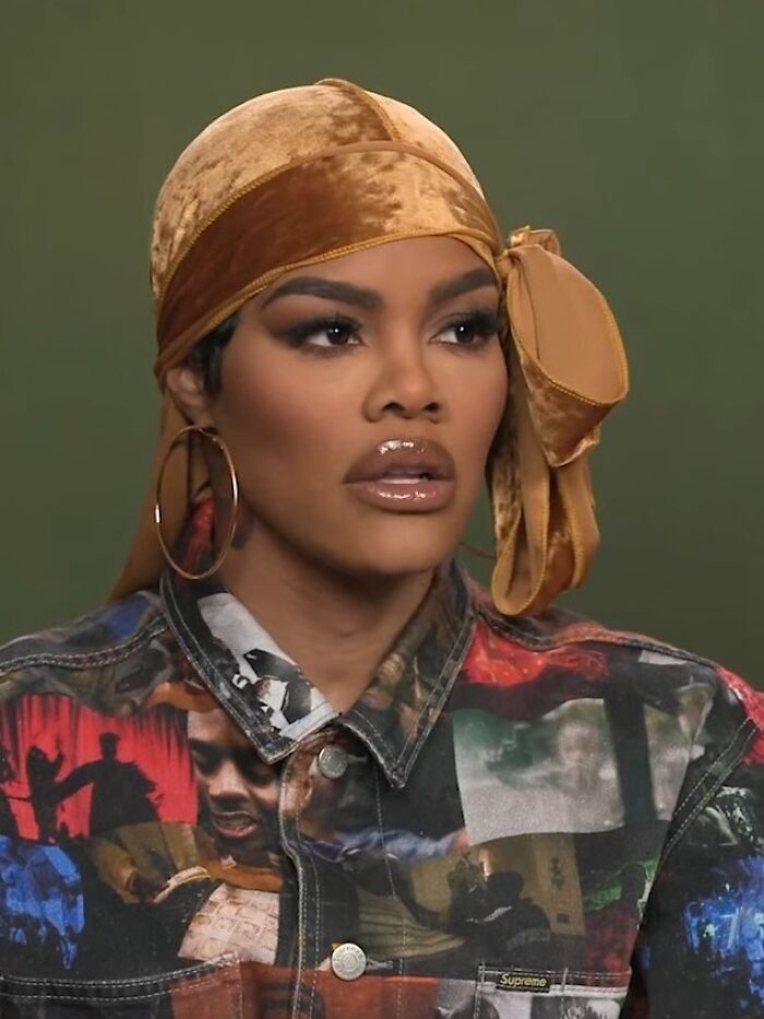 Teyana Taylor wearing a patterned jacket and gold headscarf, looking focused during an interview session.
