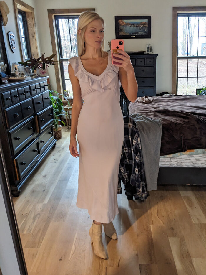 Woman wearing a vintage dress in a bright bedroom, showcasing cool unexpected secondhand store finds.