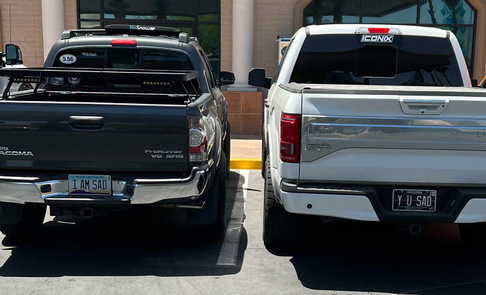 Two trucks parked side by side with personalized license plates reading I AM SAD and YU SAD, humorous license plates.