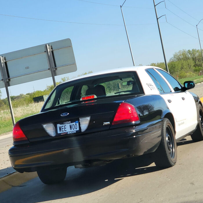 Black and white police car with a hilarious personalized license plate that made strangers do double takes on a sunny day.