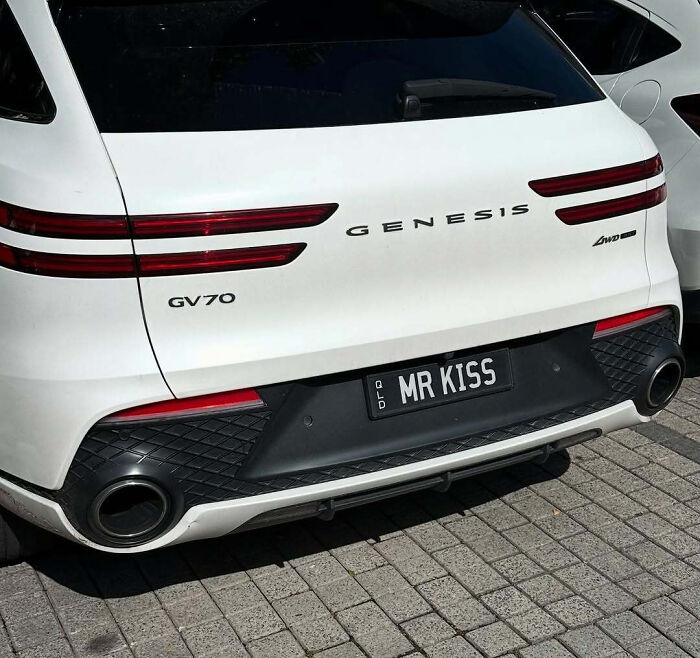 White Genesis GV70 with a hilarious personalized license plate reading MR KISS parked on a paved street.