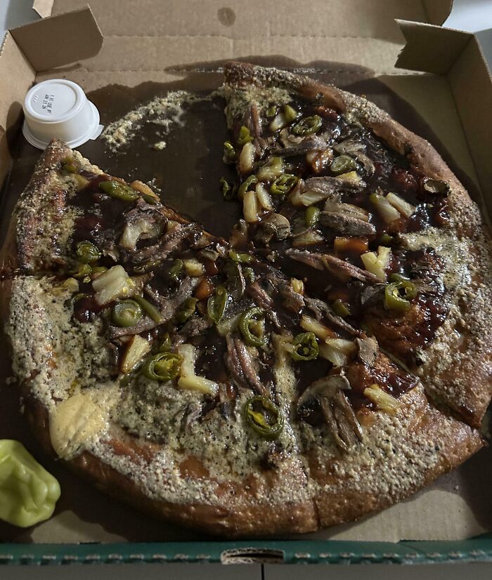 Overcooked pizza with unappealing toppings and melted cheese that looks nothing like the menu photos in a delivery box.