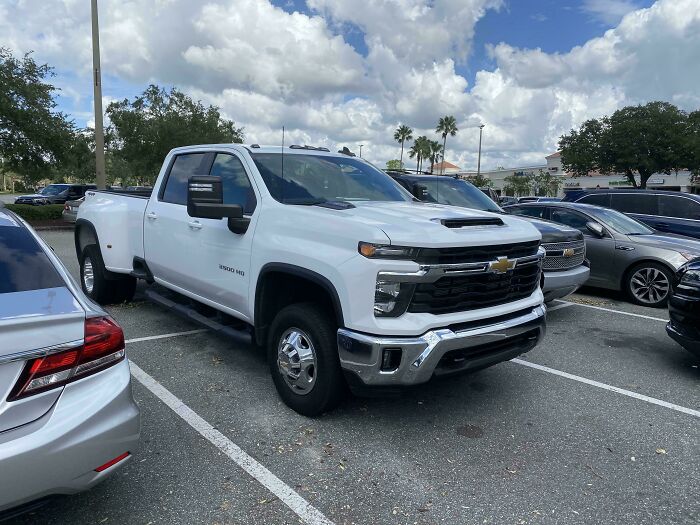 White Chevrolet Silverado 3500 HD pickup truck parked in a lot under a partly cloudy blue sky.