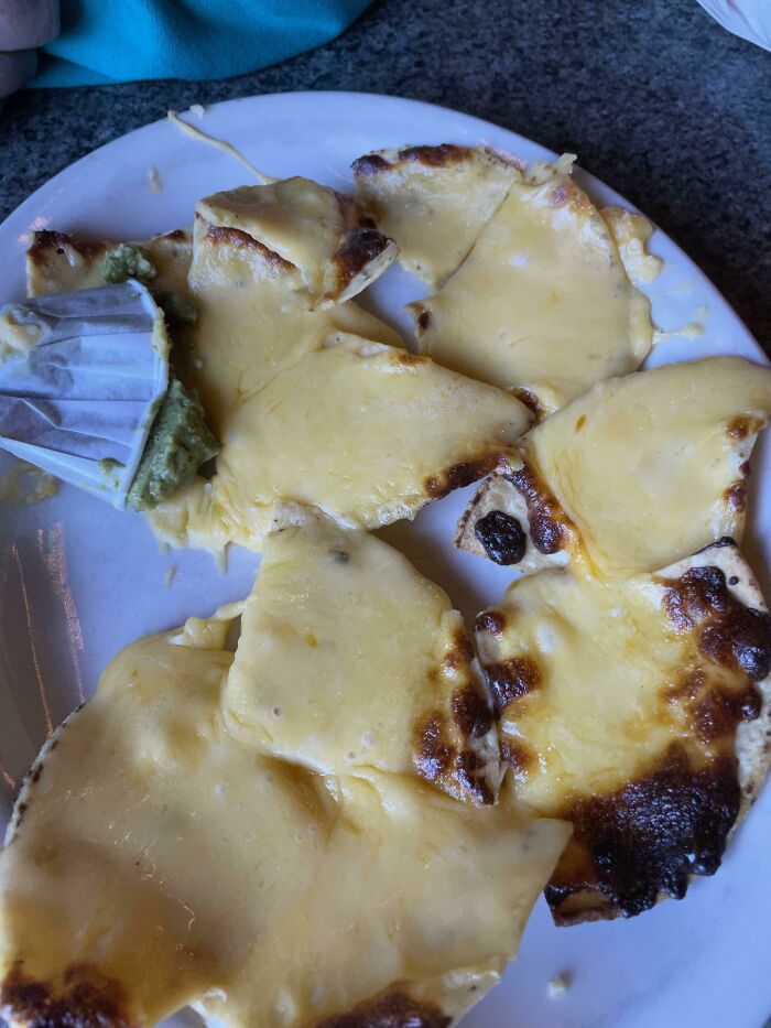 Plate of cheesy flatbread with unevenly melted and burnt cheese, an example of outrageous meals that look nothing like menu photos.