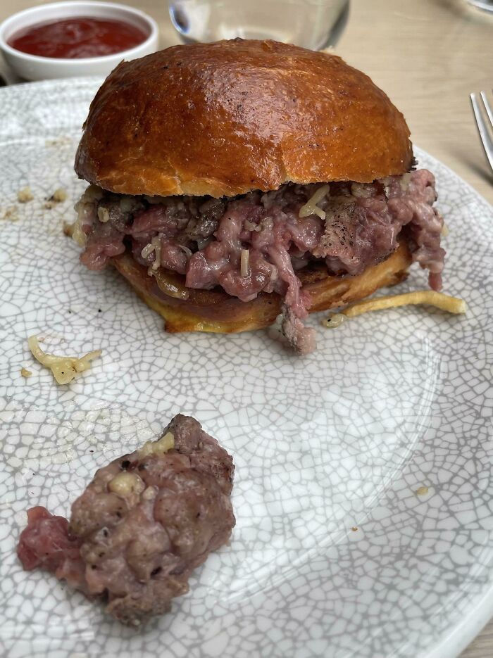 Burger with undercooked meat and melted cheese on a plate, an example of outrageous meals that look nothing like menu photos.