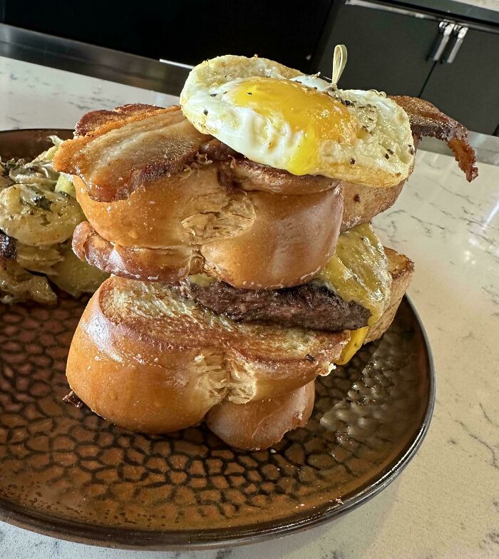 Stacked burger with bacon and fried egg on a rustic plate, an outrageous meal that looks nothing like the menu photos.