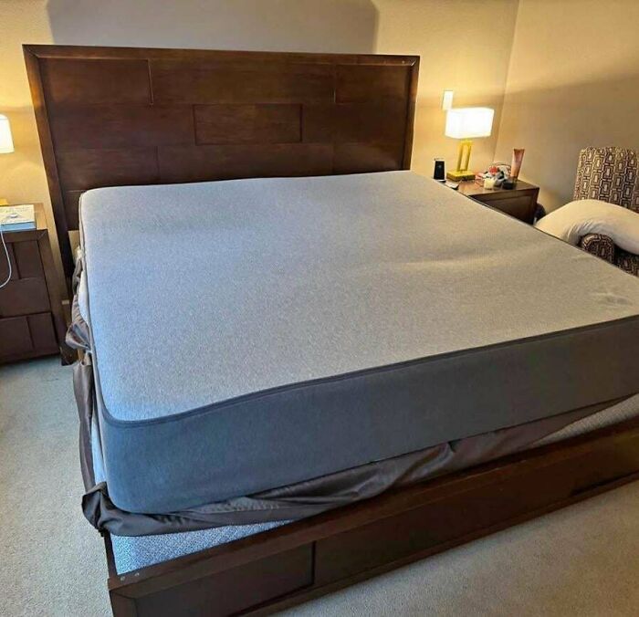 Unmade bed with a mattress, wooden headboard, nightstands with lamps, in a softly lit bedroom setting.