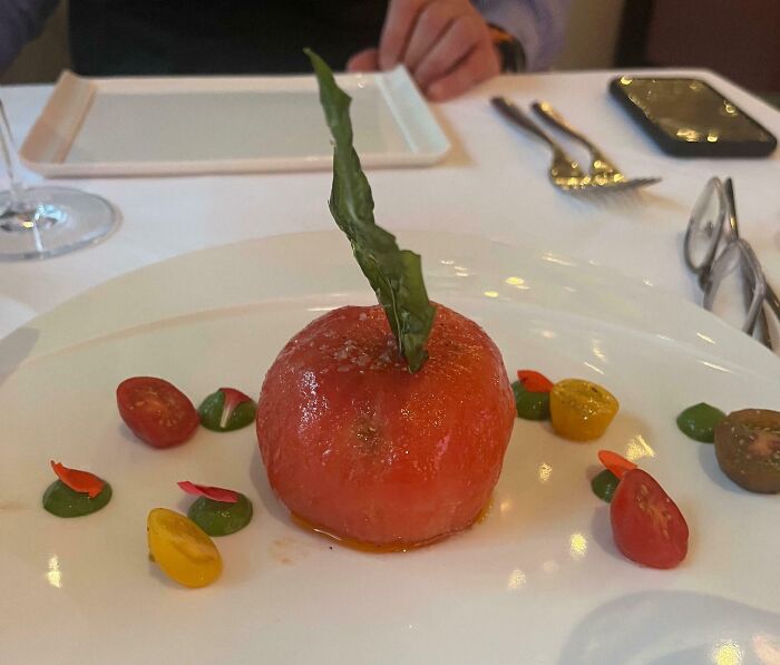 Plated meal featuring a peeled tomato with basil leaf and cherry tomato halves, showcasing outrageous meals not like menu photos.