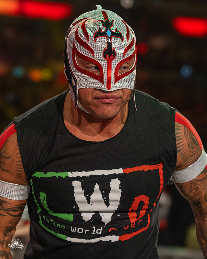 Rey Mysterio wearing a silver and red mask with a black Latino World Order shirt during a wrestling event.