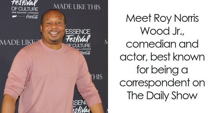 Roy Wood Jr. smiling at Essence Festival of Culture event, wearing a pink sweater and standing against a black backdrop.