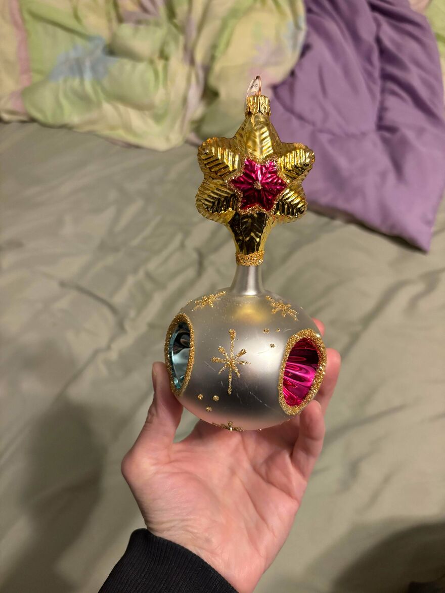 Hand holding a vintage Christmas decoration with a gold star and colorful reflective details, showcasing nostalgic holiday charm.