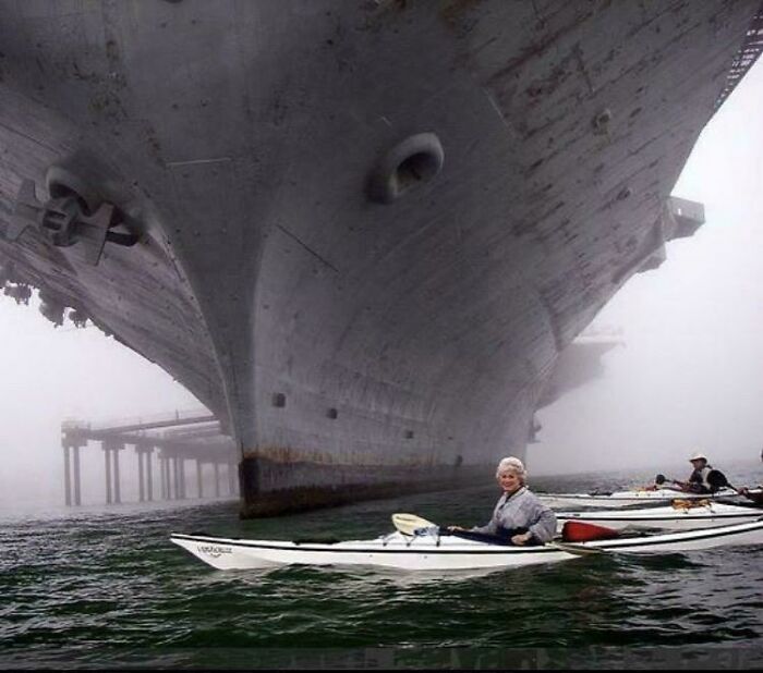 Kayakers paddling near the massive hull of a ship, showcasing an intense example of megalophobia-inducing scale and size.