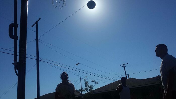 Three people playing basketball outdoors at sunset with the ball perfectly aligned with the sun in a funny, interesting, and weird moment.