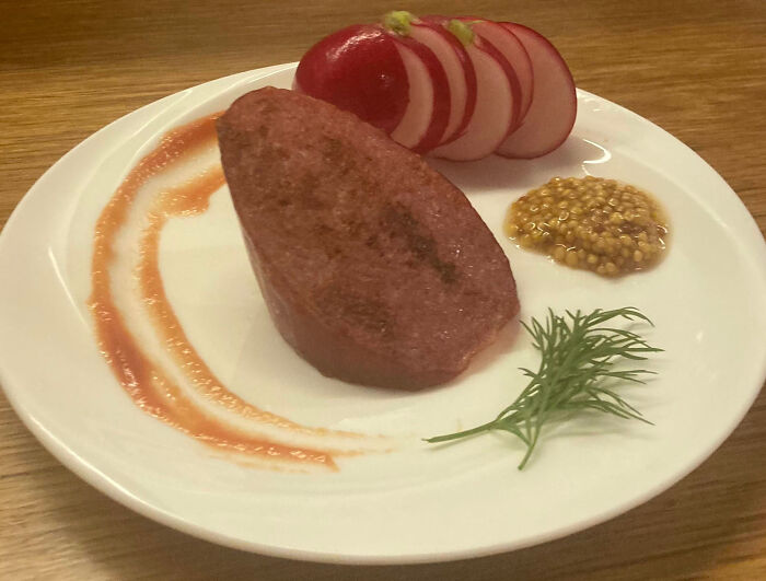 Outrageous meal with a thick meat slice, sliced radishes, mustard seeds, dill, and sauce on a white plate
